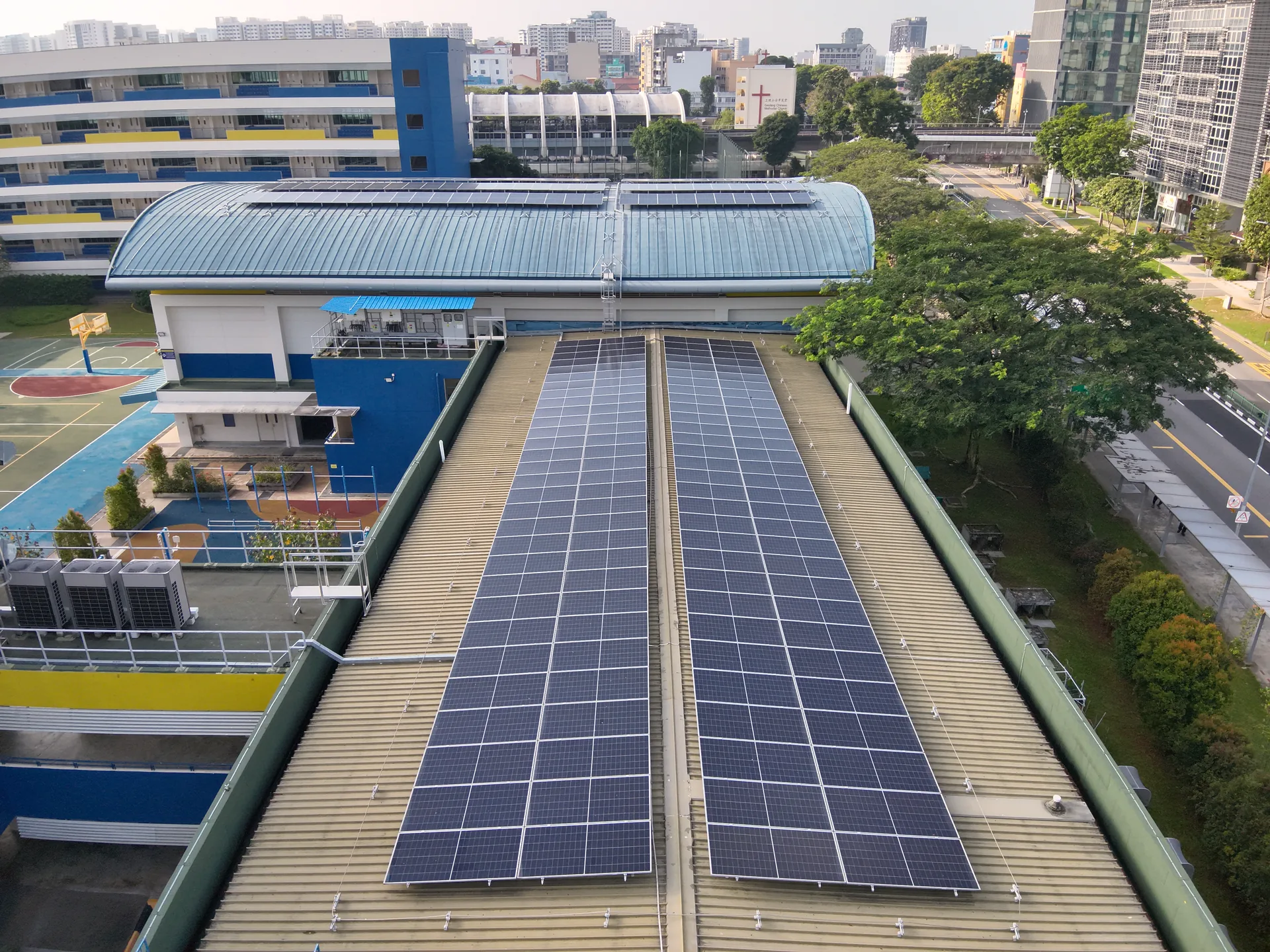 MOE schools estate — Geylang Methodist Sec School curved-roof PV array with sports field and Singapore skyline